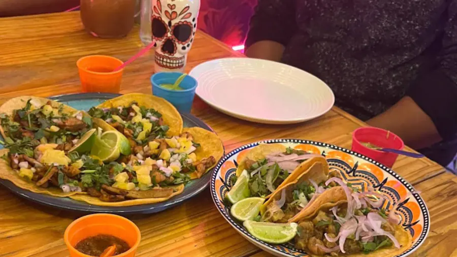 Tacos de pastor y de suadero en platos de talavera junto a un vaso de calavera